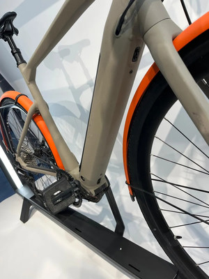 Detail eines Elektrofahrrads mit orangefarbenen Schutzblechen und schwarzen Pedalen.