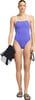 Eine Frau in einem lila Badeanzug hält ein Handtuch und eine Schwimmbrille.