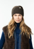 Eine Frau mit einer braunen Mütze und einer pelzigen Weste trägt einen blauen Rollkragenpullover.