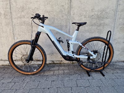 Ein hellblaues E-Bike mit braunen Reifen steht auf einem Ständer vor einer Wand.