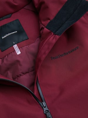 Detail einer dunkelroten Peak Performance Jacke mit Reißverschluss und Logo. Detail einer dunkelroten Peak Performance Jacke mit Reißverschluss und Logo.