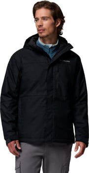 Ein Mann in einer schwarzen Columbia-Jacke mit Kapuze und grauer Hose mit Taschen.