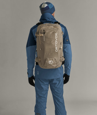 Ein Mann in Skibekleidung mit Rucksack und blauer Mütze.
