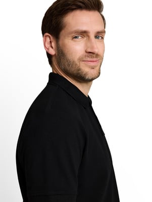 Egy fekete galléros pólóban lévő férfi enyhe mosollyal jobbra néz. Egy fekete galléros pólóban lévő férfi enyhe mosollyal jobbra néz.