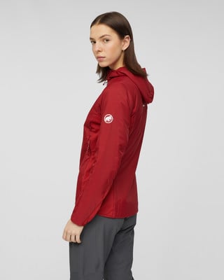 Eine Frau in einer roten Kapuzenjacke und grauer Hose vor grauem Hintergrund.