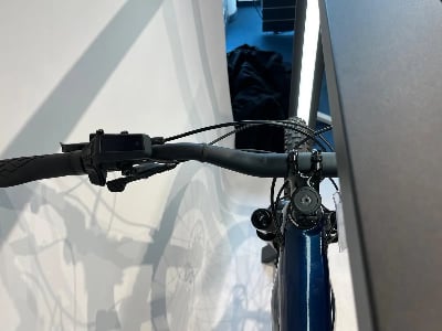 Detail des Lenkers eines dunkelblauen Fahrrads mit Display und Bremshebeln.