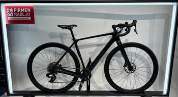 Ein schwarzes Gravelbike auf einem Ausstellungsständer mit Werbung