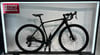 Ein schwarzes Gravelbike auf einem Ausstellungsständer mit Werbung