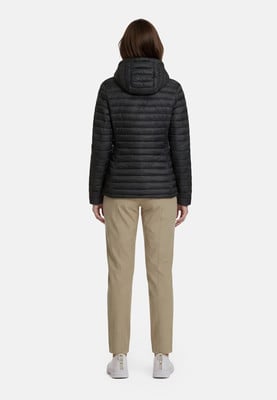 Eine Frau in einer schwarzen Daunenjacke mit Kapuze und beiger Hose steht rückwärts.