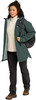 Frau in grüner Jacke und schwarzer Hose mit Rucksack.