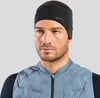 Ein Mann mit schwarzem Stirnband und blauer Weste vor grauem Hintergrund.