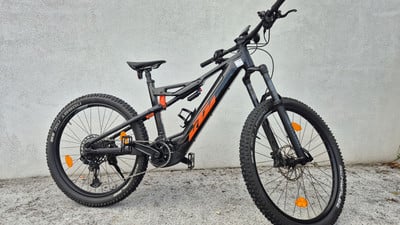 Ein schwarzes KTM E-Bike mit orangefarbenen Details steht vor einer Wand. Ein schwarzes KTM E-Bike mit orangefarbenen Details steht vor einer Wand.