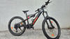 Ein schwarzes KTM E-Bike mit orangefarbenen Details steht vor einer Wand.