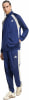 Ein Mann in einem blauen Adidas Trainingsanzug mit beigen Streifen und Logo.