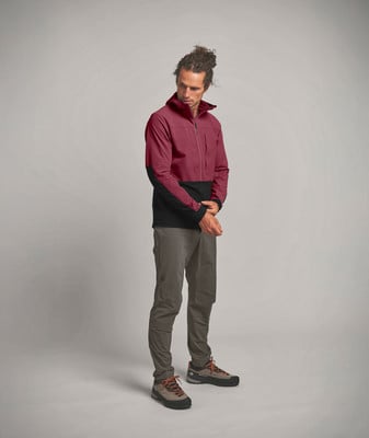Ein Mann in einer dunkelroten Jacke und grauer Hose steht vor einem grauen Hintergrund. Ein Mann in einer dunkelroten Jacke und grauer Hose steht vor einem grauen Hintergrund.