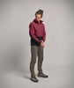 Ein Mann in einer dunkelroten Jacke und grauer Hose steht vor einem grauen Hintergrund.