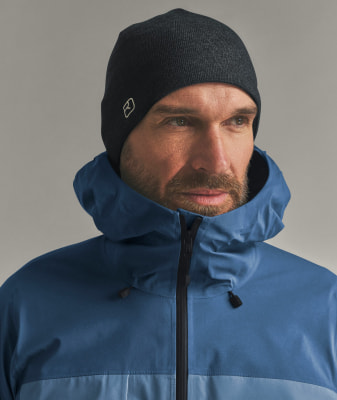 Ein Mann mit dunkler Mütze und blauer Jacke mit zugezogener Kapuze. Ein Mann mit dunkler Mütze und blauer Jacke mit zugezogener Kapuze.