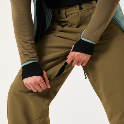Detail eines Mannes in Khaki-Hose und olivgrüner Jacke mit schwarzen Ärmeln.