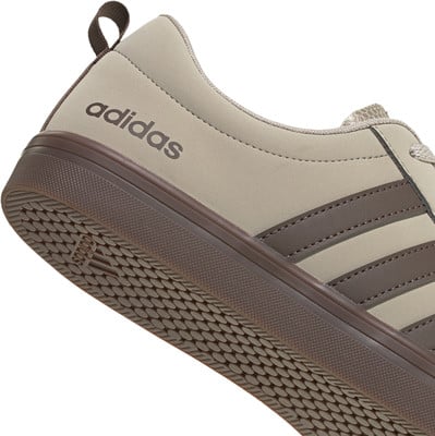 Detail eines Adidas-Schuhs mit braunen Streifen und Logo auf beigem Hintergrund. Detail eines Adidas-Schuhs mit braunen Streifen und Logo auf beigem Hintergrund.