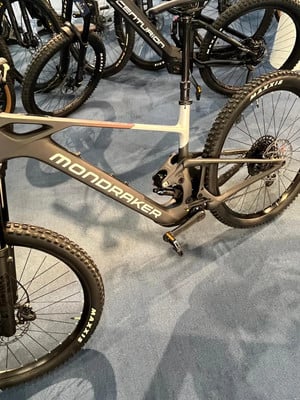 Detail eines Mountainbikes mit der Aufschrift MONDRAKER und Federung auf blauem Teppich. Detail eines Mountainbikes mit der Aufschrift MONDRAKER und Federung auf blauem Teppich.