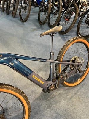 Ein blaues Trek E-Bike mit orangefarbenen Felgen auf blauem Teppich.