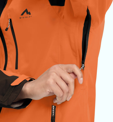 Nahaufnahme einer orangefarbenen Jacke mit McKinley-Logo und einer Hand in einer Tasche. Nahaufnahme einer orangefarbenen Jacke mit McKinley-Logo und einer Hand in einer Tasche.