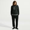 Ein Mann in einem schwarzen Nike Hoodie und Hose steht vor weißem Hintergrund.