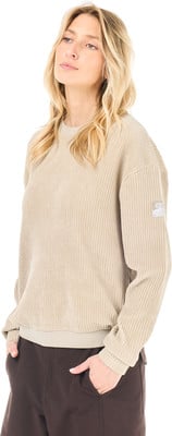 Eine Frau in einem beigen Cordpullover und braunen Hosen mit den Händen in den Taschen. Eine Frau in einem beigen Cordpullover und braunen Hosen mit den Händen in den Taschen.