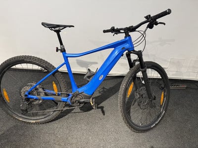 Ein blaues E-Bike mit Federung und schwarzen Rädern steht auf einem Teppich.