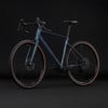 Ein blauer Gravelbike mit braunen Reifen vor schwarzem Hintergrund.
