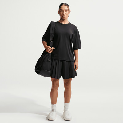 Frau in schwarzem T-Shirt und Rock mit Tasche über der Schulter.